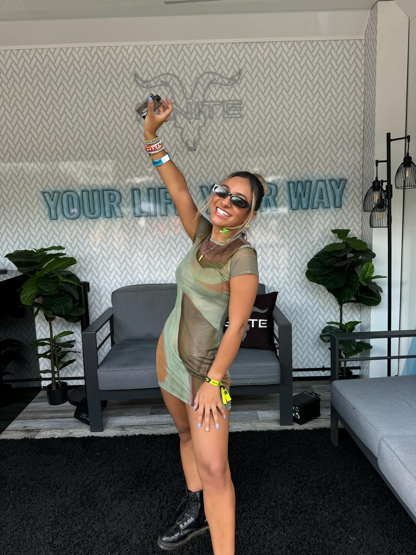 Woman with sunglasses and a raised arm in front of the wall reading Your life, your way in an IGNITE lounge